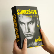 Hardcover of Bono's autobiography "Surrender," featuring 40 songs and personal stories, published by Hutchinson Heinemann.