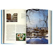 Hardcover book "The New York Times Explorer: 100 Trips Around the World" by Taschen, featuring colorful travel images on the cover.