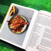 Hardcover book titled "Original Flava: Caribbean Recipes From Home" by Craig McAnuff, featuring colorful cover art on a wooden table.